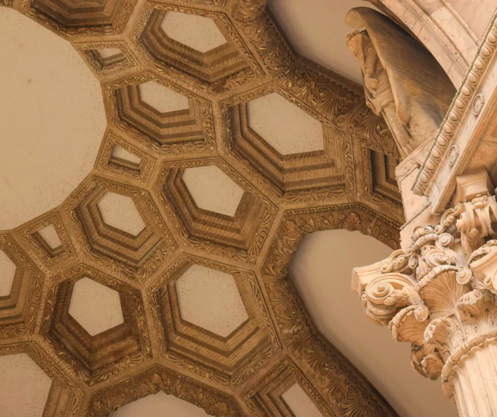 Ornate ceiling and column detail in classical architecture, showcasing intricate geometric patterns and carved designs.