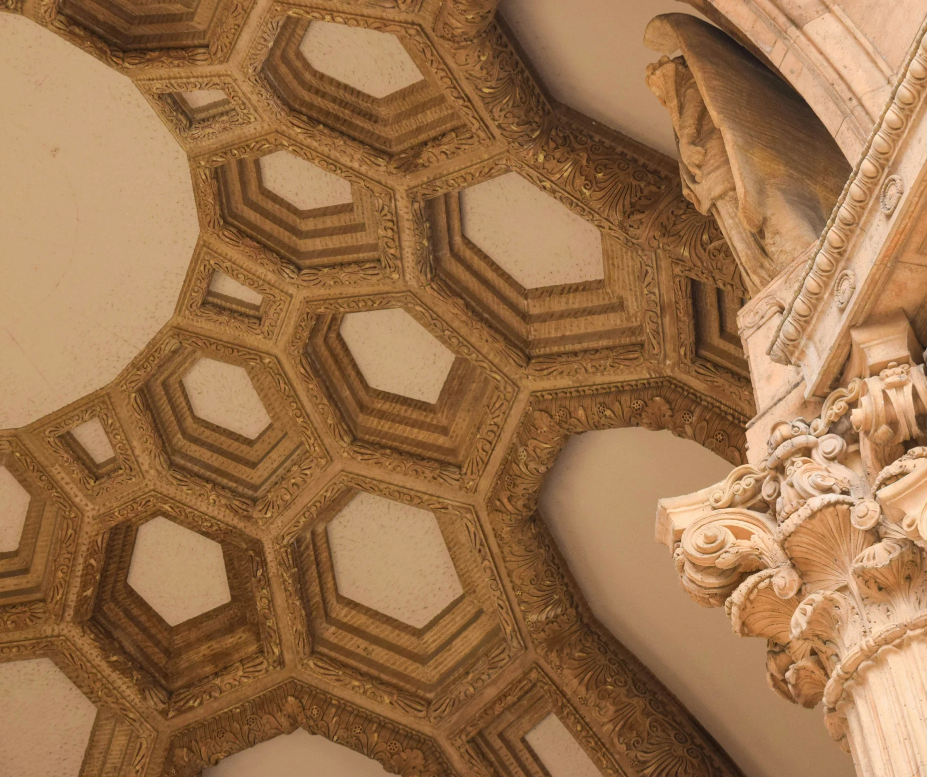 Ornate ceiling and column detail in classical architecture, showcasing intricate geometric patterns and carved designs.