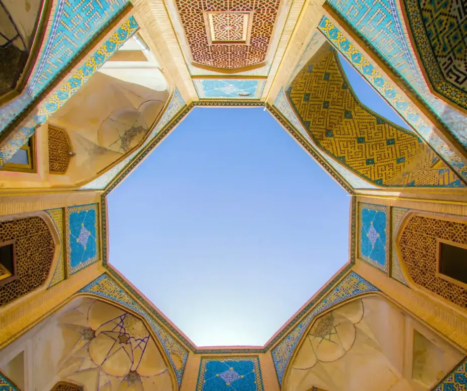 Intricate geometric ceiling with vibrant patterns and blue sky view in traditional Middle Eastern architecture.