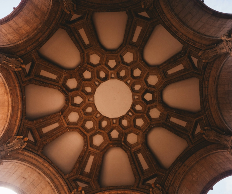 Ornate architectural dome ceiling with geometric patterns, seen from below, showcasing intricate design and structure.